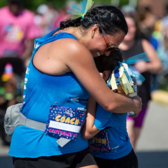 Coach in a blue shirt hugging a Girls on the Run participant